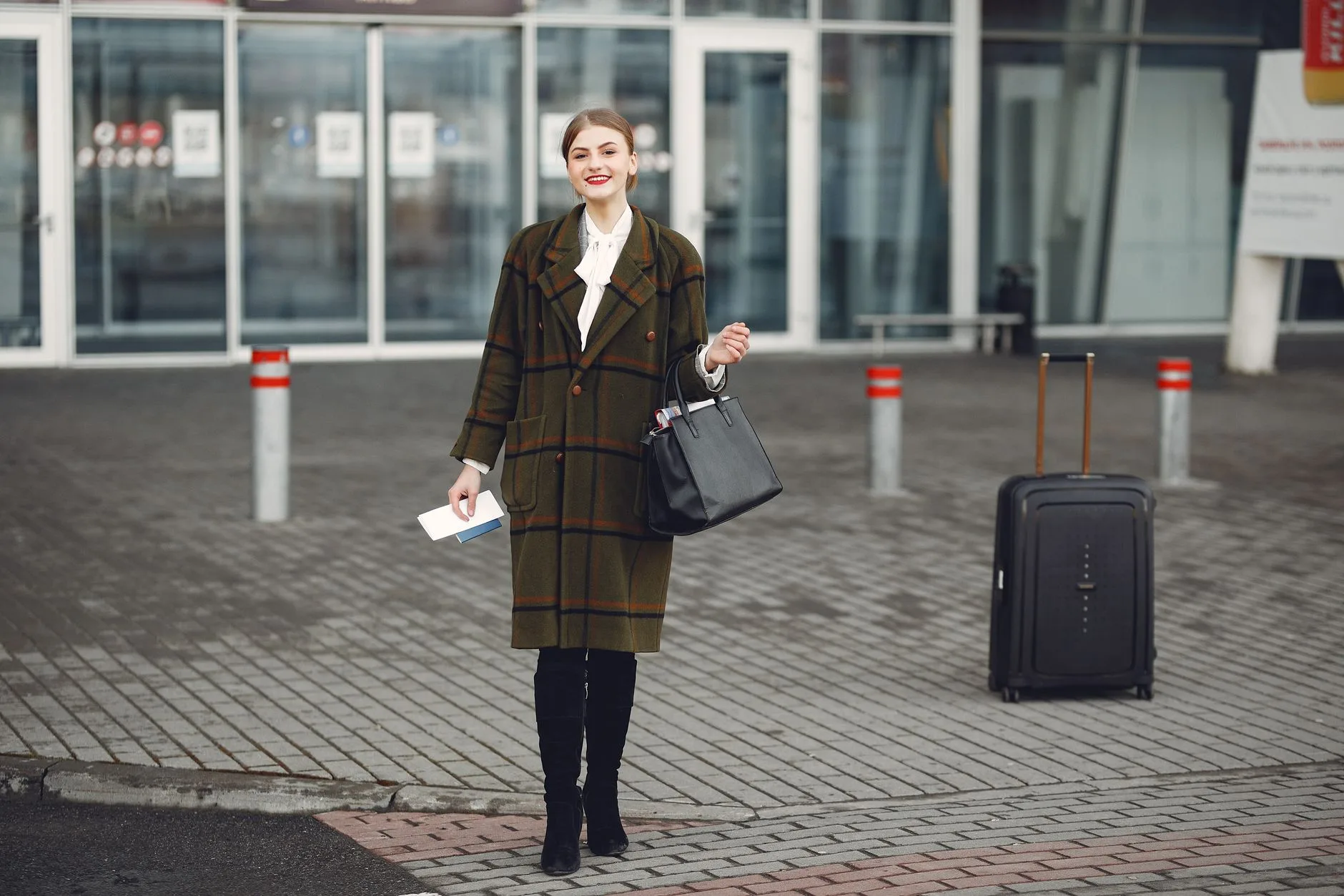 Voyageuse devant un aéroport avec sa valise et ses documents de voyage